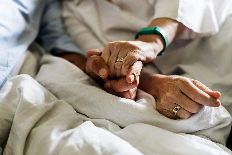 Close-up of two people holding hands in a comforting hospital setting