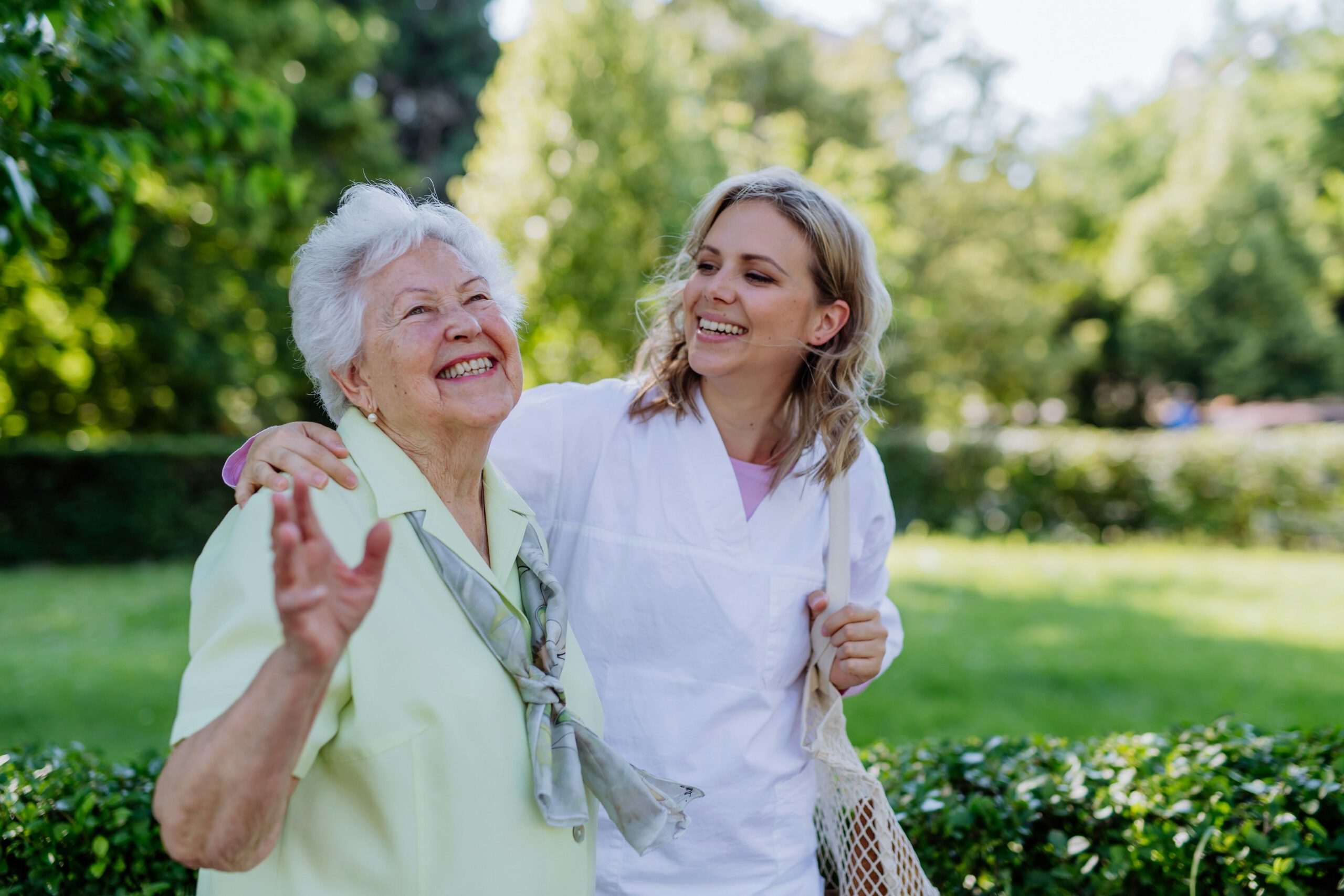 Caregiver walking arm-in-arm with a smiling elderly woman outdoors