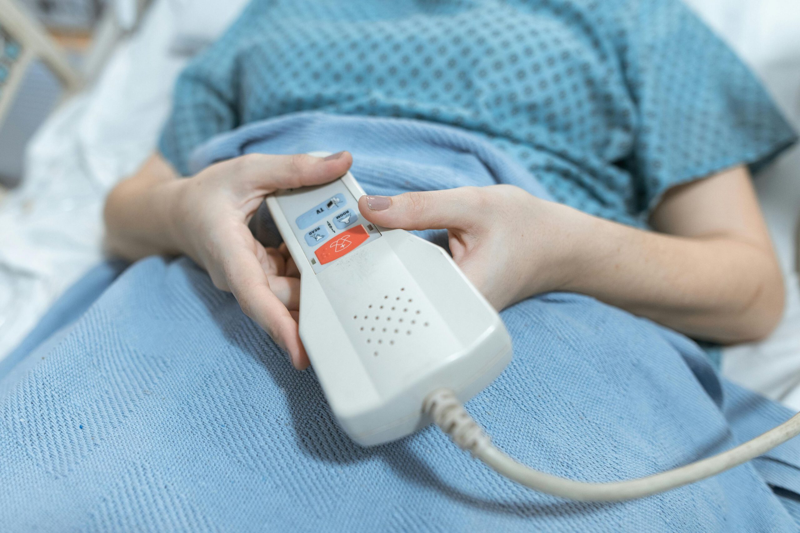Patient holding a call button device while lying in a hospital bed