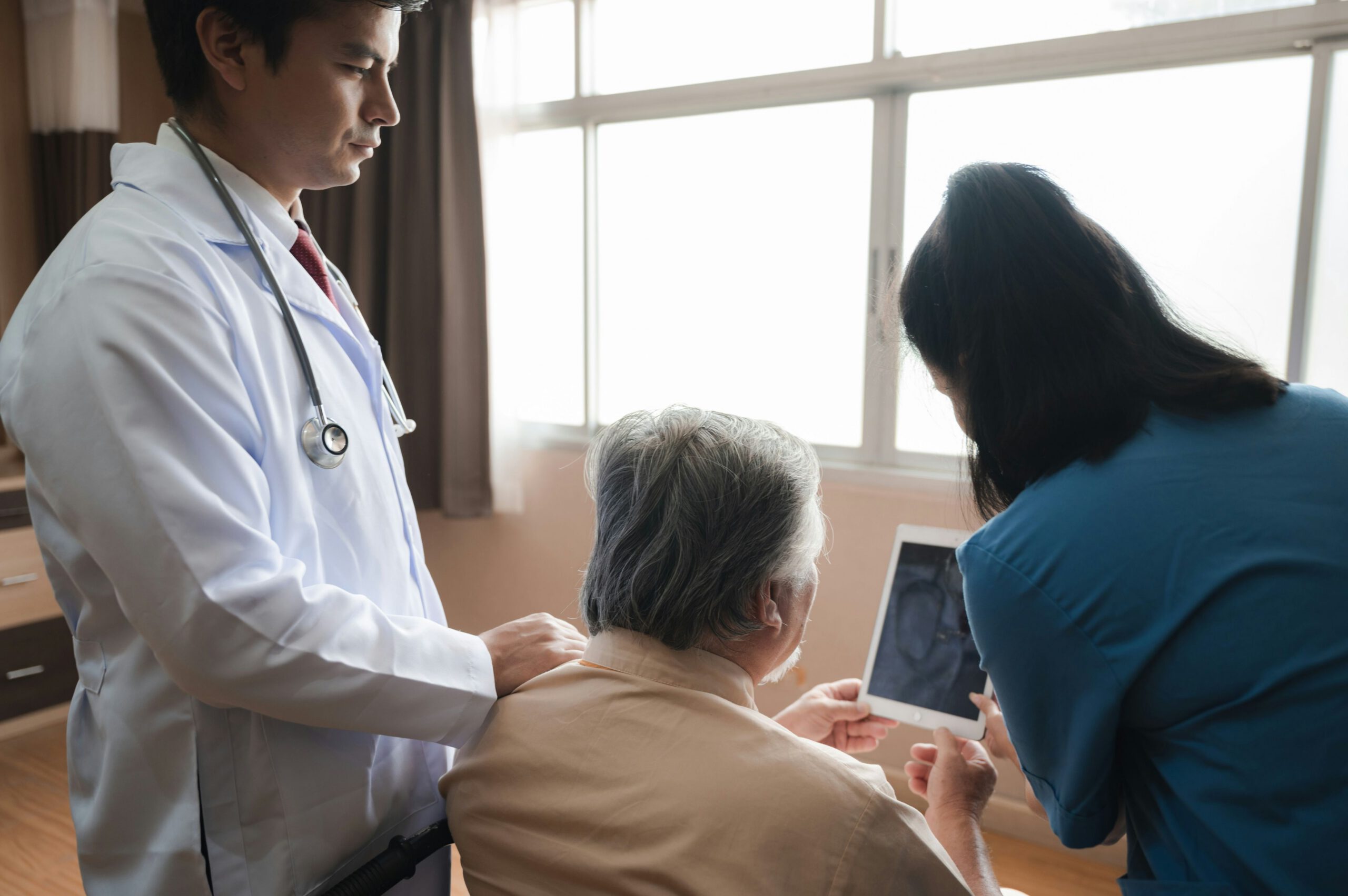 Doctor and caregiver reviewing a tablet with an older patient by a window