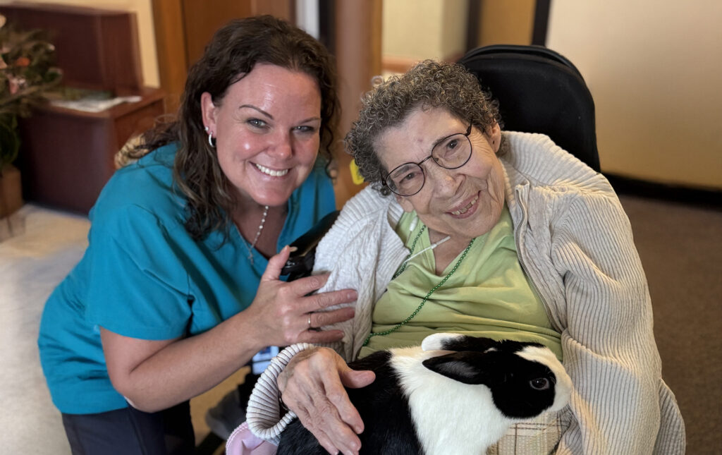 Caregiver sitting close to an older woman who is holding a bunny, sharing a warm and personal moment
