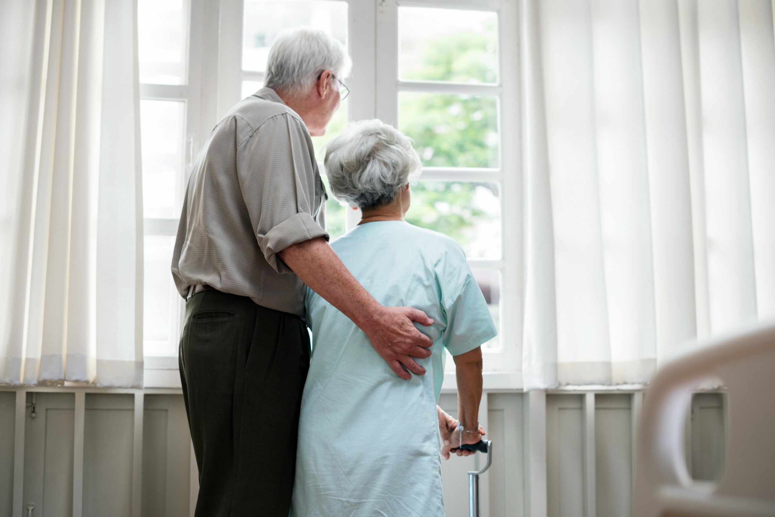 Older couple standing together by a window, sharing a quiet moment