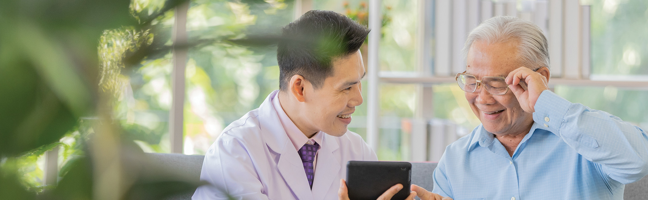 Care provider sitting with an older man and sharing something on a tablet, creating a moment of connection and engagement