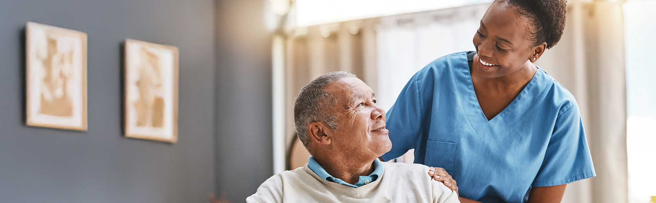 Caregiver standing beside an older man with a reassuring hand on his shoulder, sharing a supportive and encouraging moment