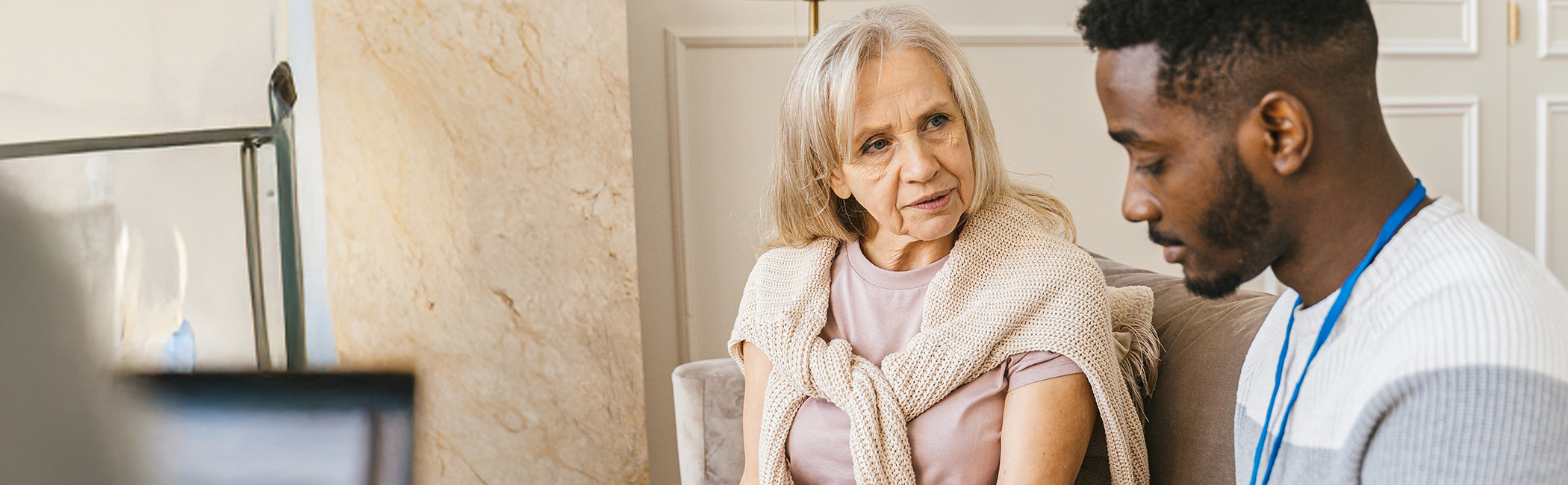 Caregiver sitting beside an older woman, listening closely and providing thoughtful, attentive support during a personal conversation