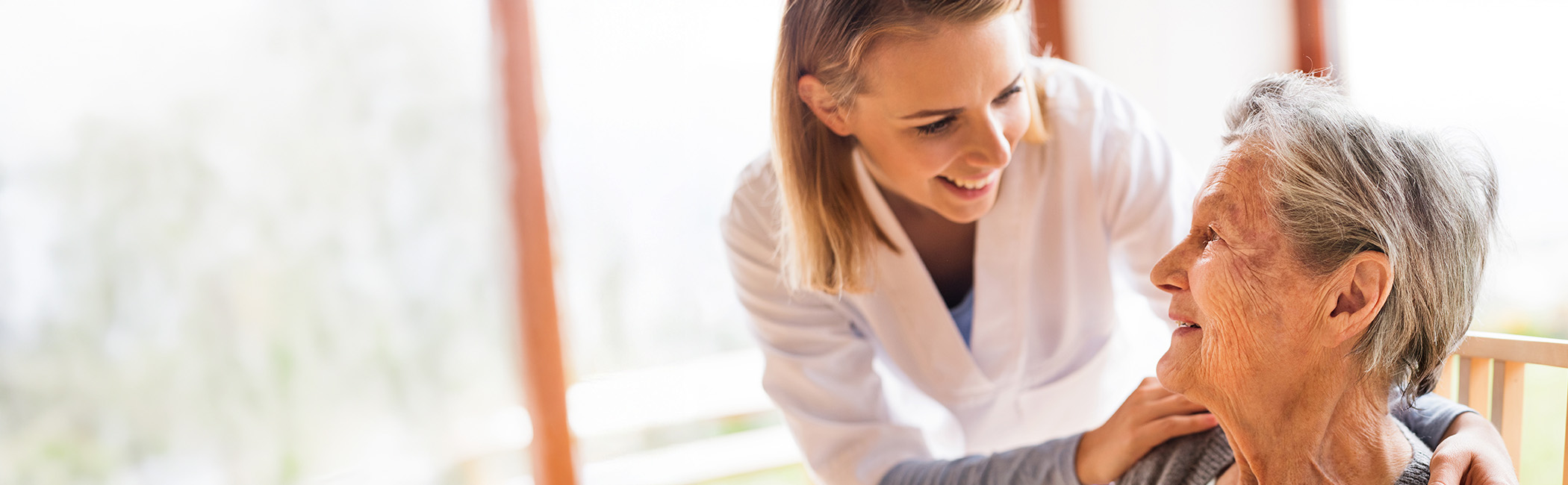 Caregiver smiling and speaking gently with an older woman, offering attentive, personal support in a calm setting