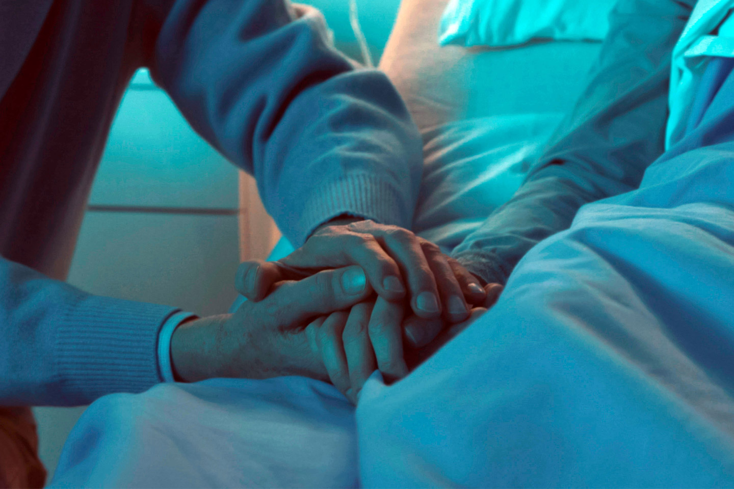 Loved one holding a patient’s hand at the bedside, offering quiet support during a vulnerable moment