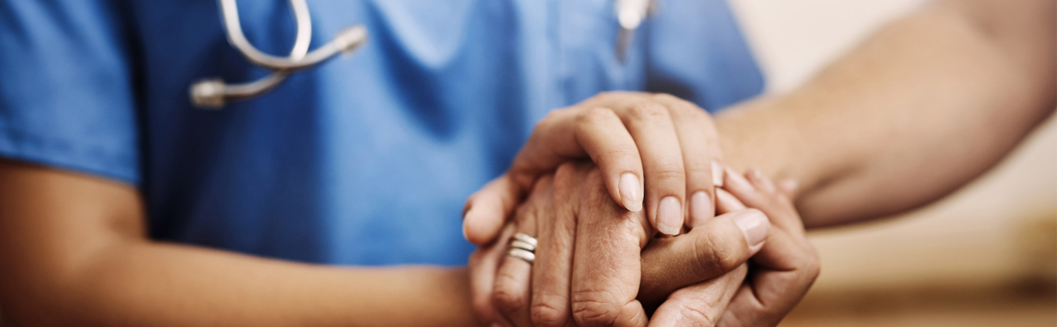 Caregiver gently holding a patient’s hands, offering steady comfort and reassurance during a moment of care