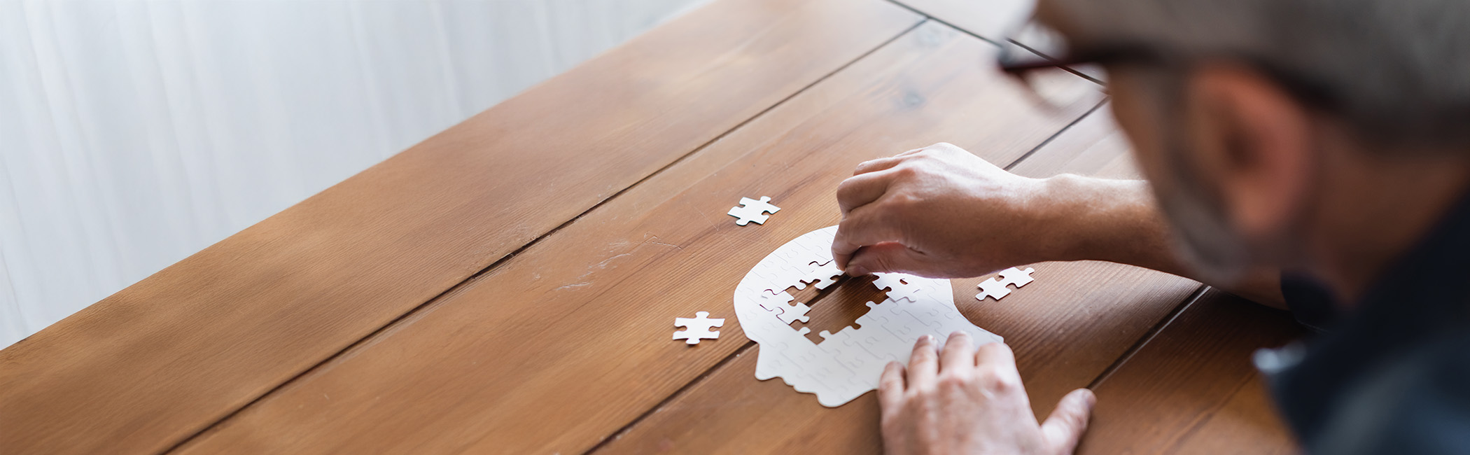 Person placing a puzzle piece into a head-shaped puzzle on a wooden table, representing memory loss and dementia care support