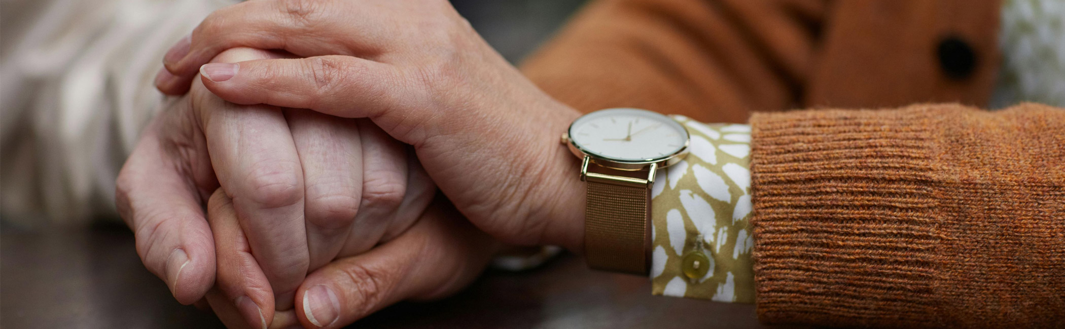 Caregiver resting a reassuring hand over another’s, offering comfort and steady support during a quiet moment