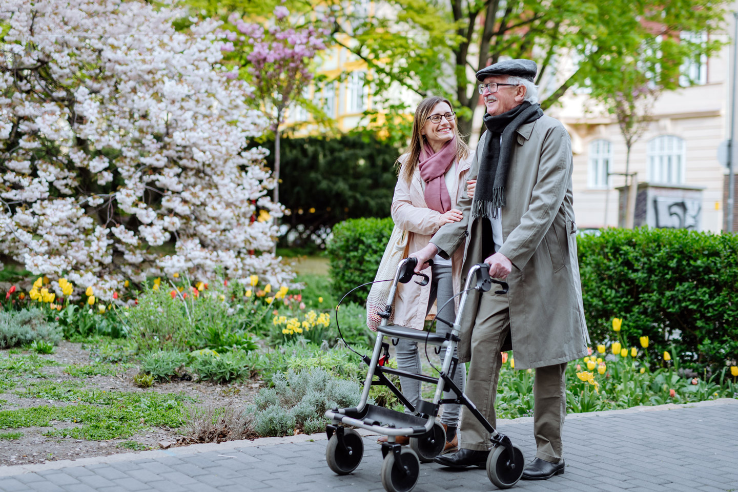 Older man using a walker while walking outdoors with a companion, enjoying fresh air and supportive companionship