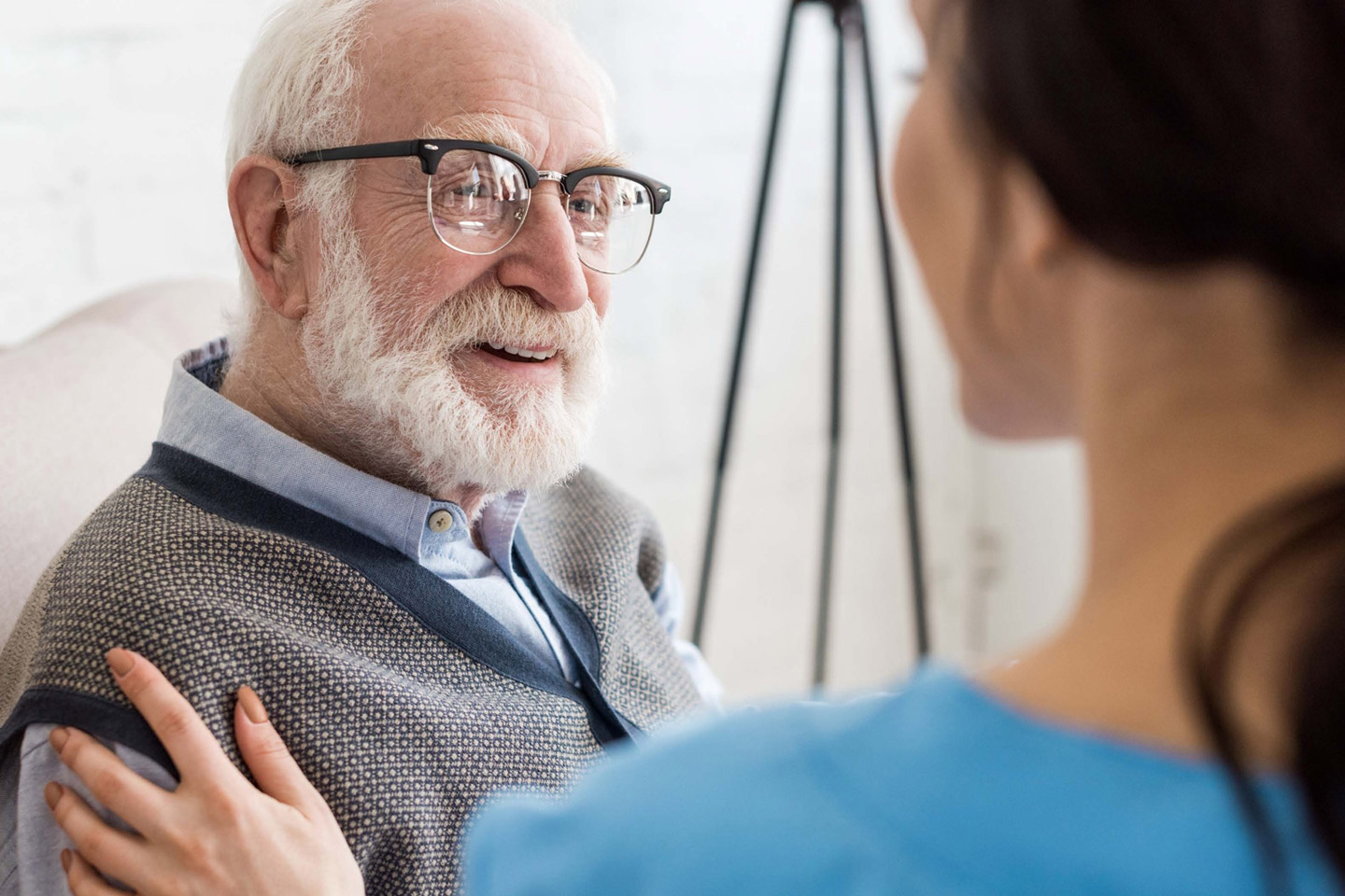 Caregiver resting a reassuring hand on an older man’s shoulder while speaking with him, offering attentive and personal support