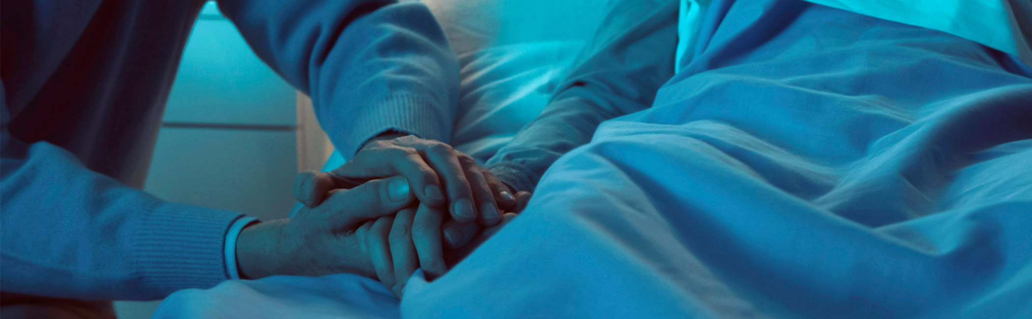 Loved one holding a patient’s hand at the bedside, offering steady comfort during a quiet, vulnerable moment