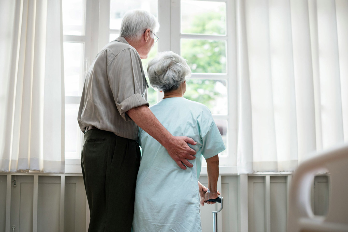 Older couple standing together by a window, sharing a quiet moment of closeness and support