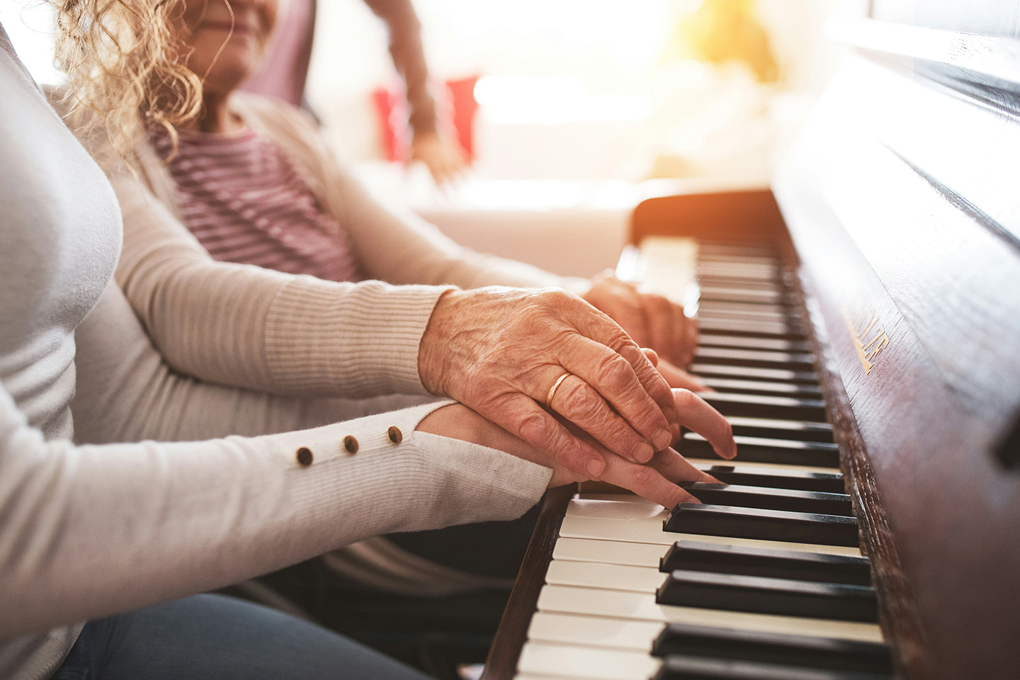 Caregiver gently guiding an older woman’s hands on a piano, sharing a familiar activity that brings comfort and connection