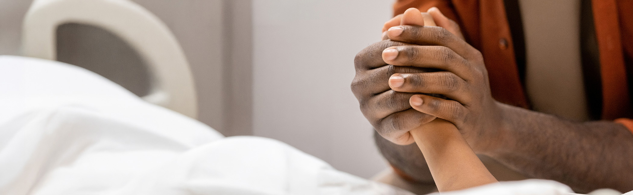 Family member holding a patient’s hand at the bedside, offering comfort and quiet support in a moment of care