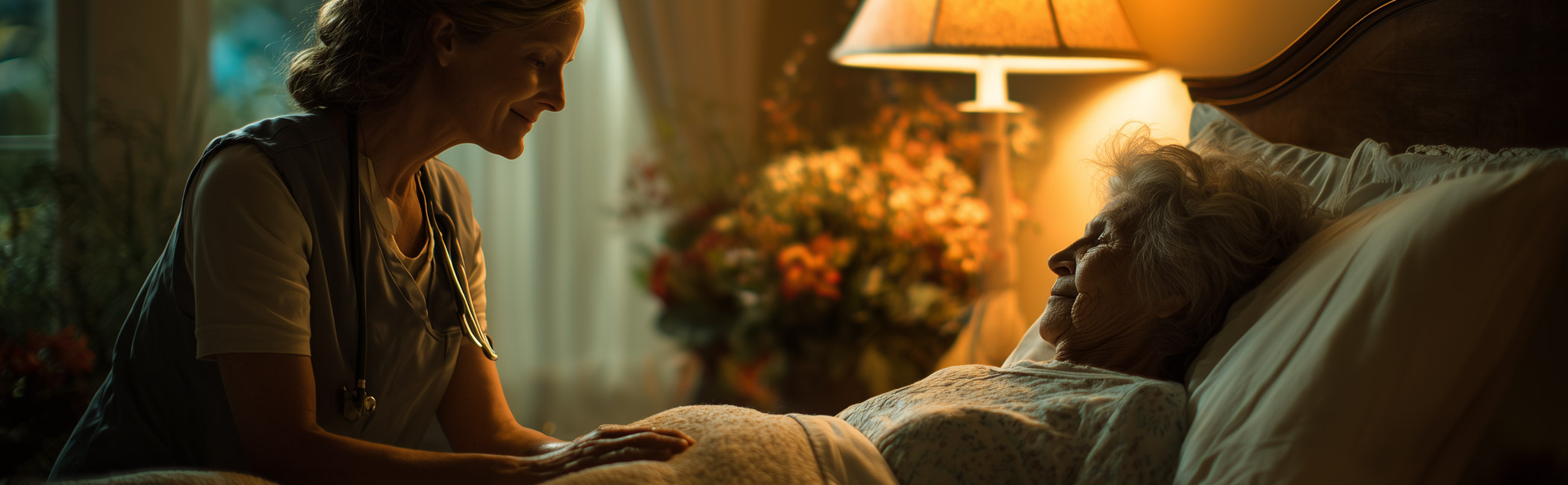 Caregiver sitting beside an older woman in bed, speaking gently and providing attentive nighttime support