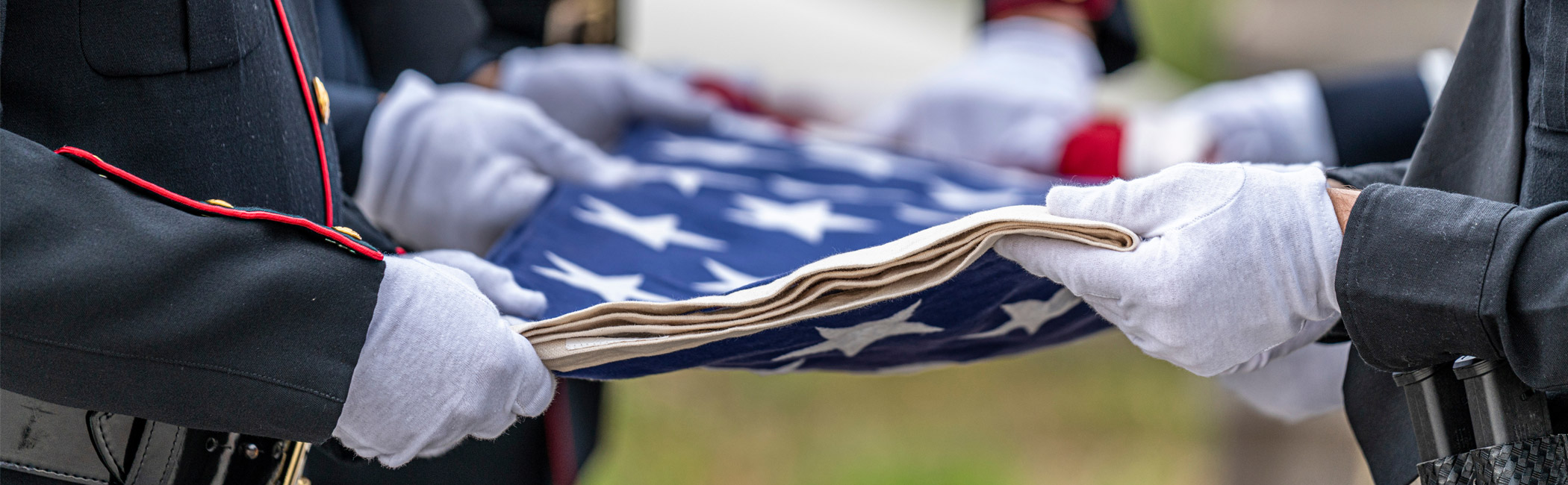 Uniformed service members carefully folding an American flag, honoring a moment of remembrance and respect
