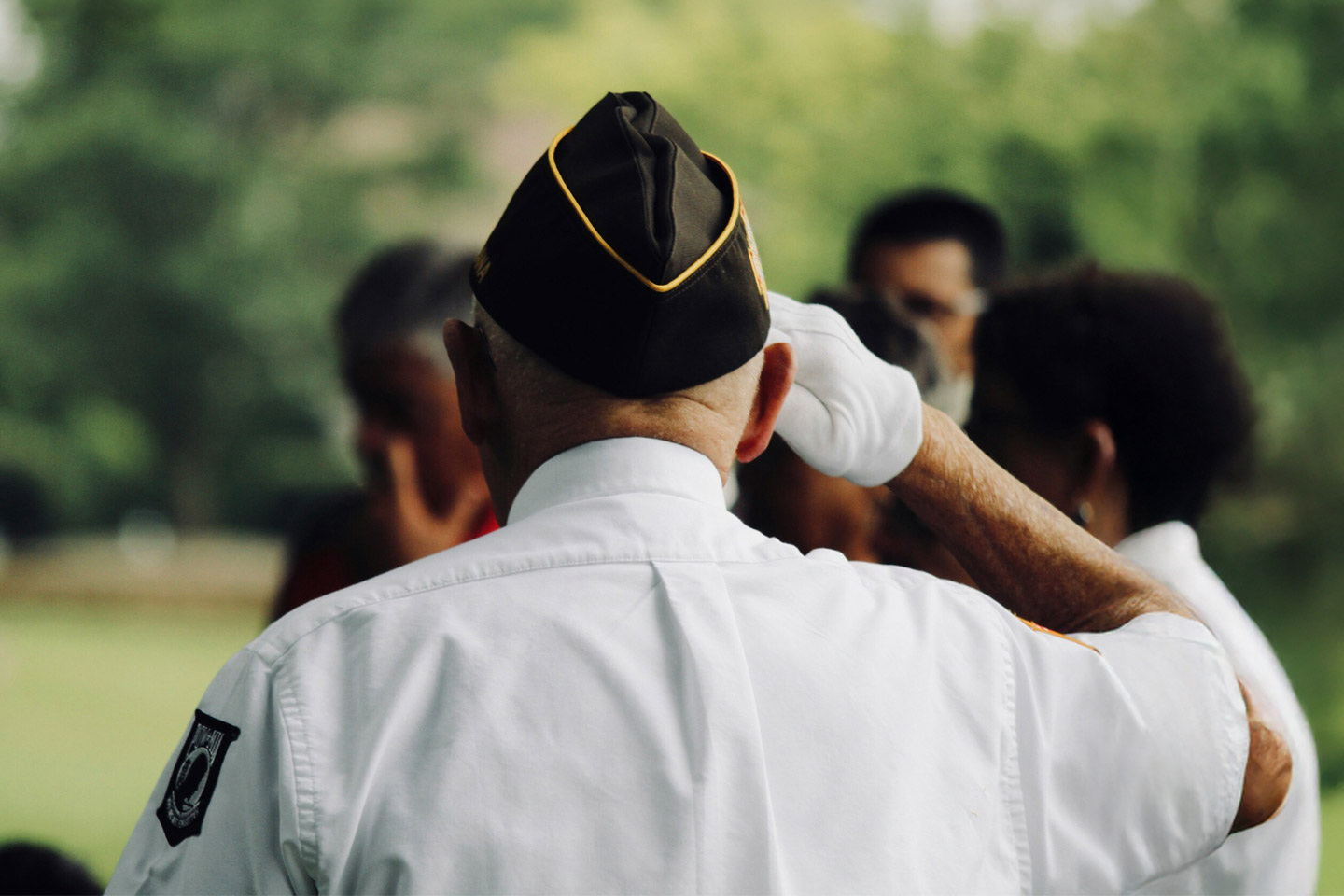 Veteran seen from behind raising a hand in salute, honoring service and shared respect in a group setting