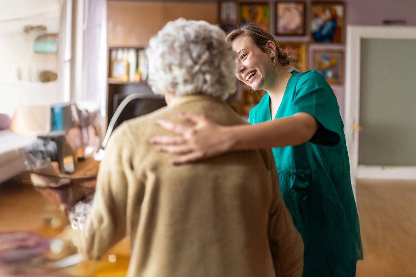 Caregiver gently guiding an older woman while walking indoors, offering steady physical support and reassurance