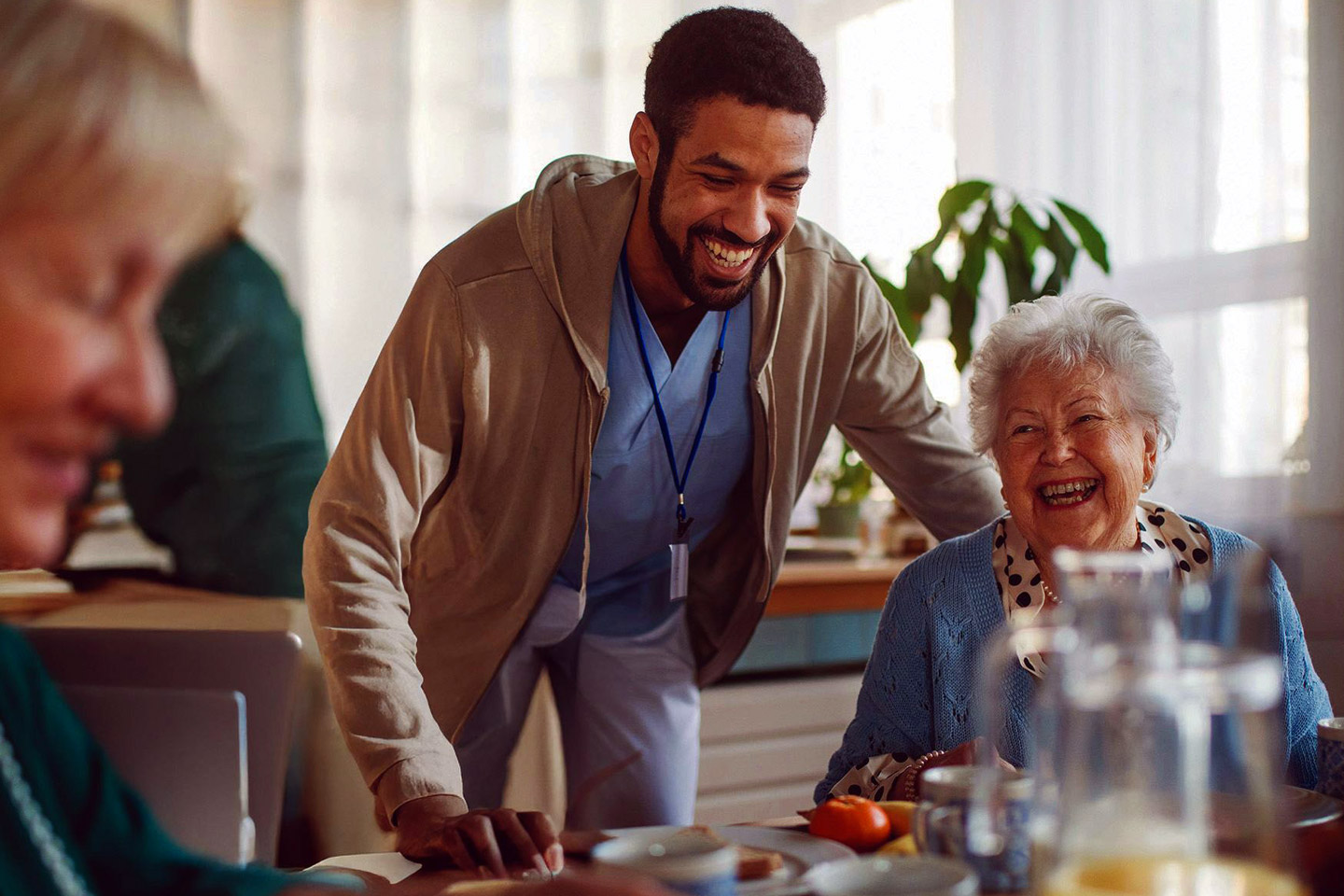 Caregiver leaning in with a smile as an older woman laughs, sharing a joyful and uplifting moment together