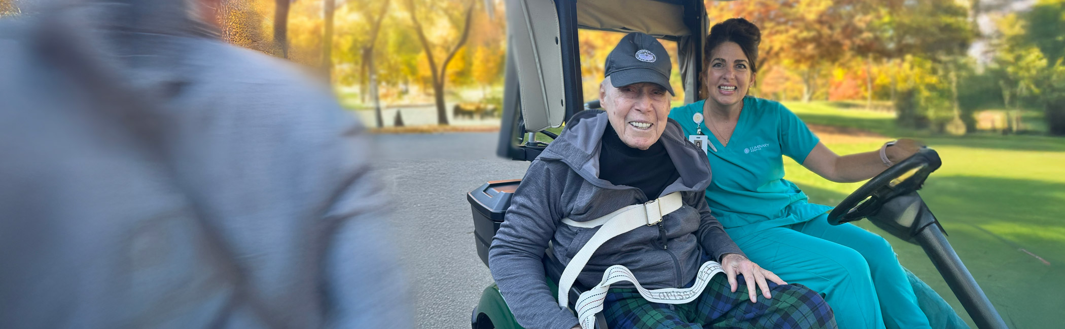 Caregiver driving an older man in a golf cart through a park, helping him enjoy time outdoors and a sense of normalcy