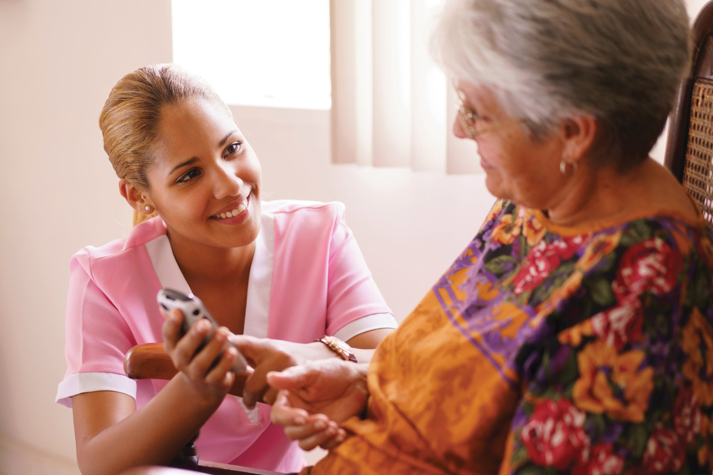 Caregiver assisting an older woman with a handheld device, offering patient guidance and one-on-one support