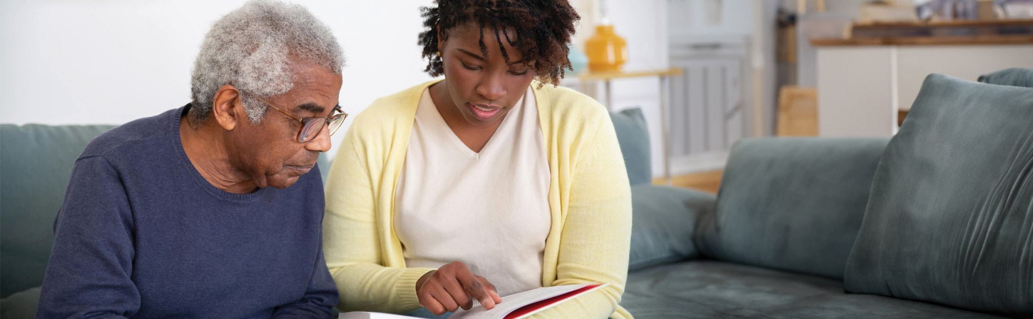 Caregiver sitting with an older man and reviewing information together, offering clear guidance and supportive conversation