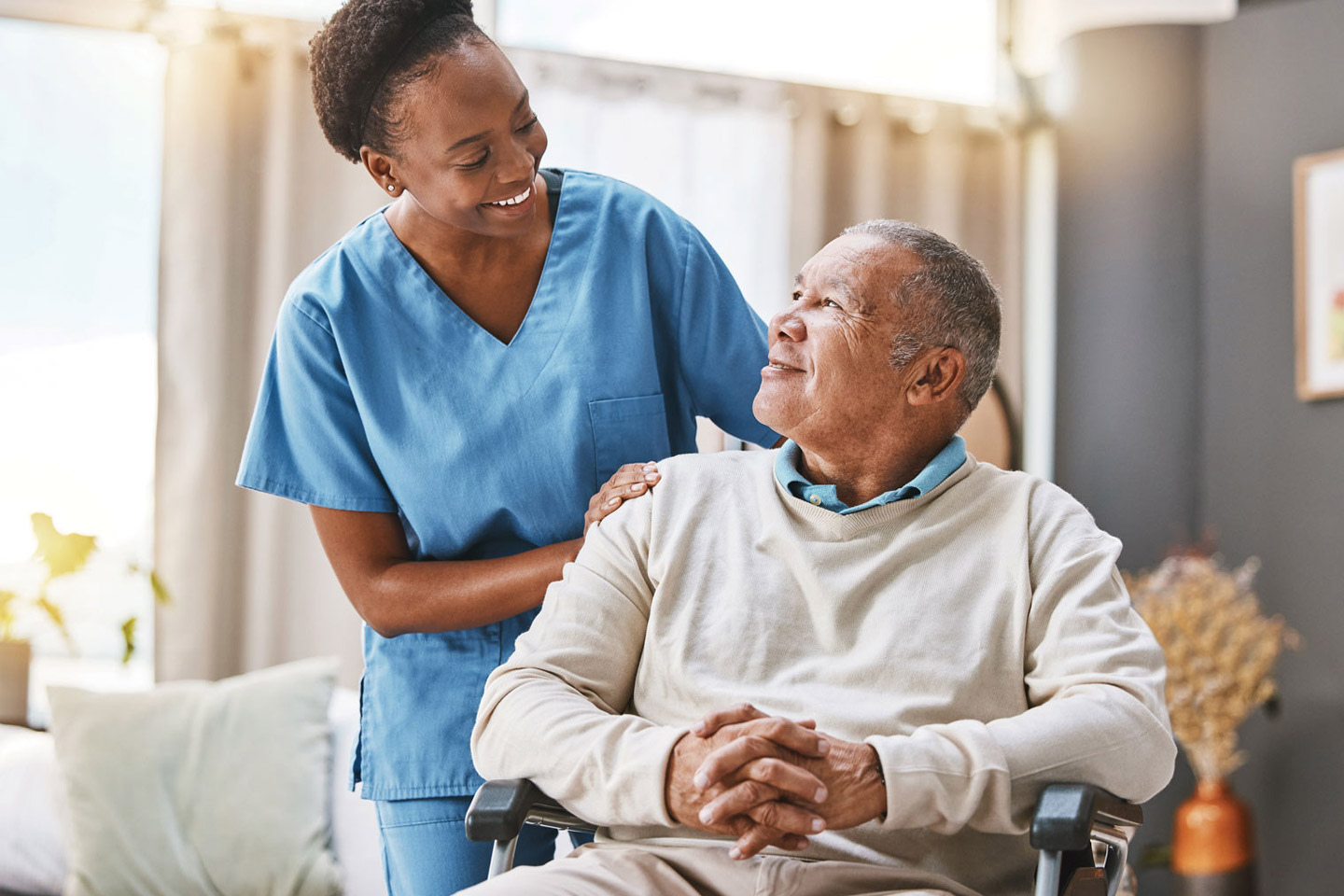 Caregiver standing beside an older man in a wheelchair with a reassuring hand on his shoulder, sharing a supportive and encouraging moment