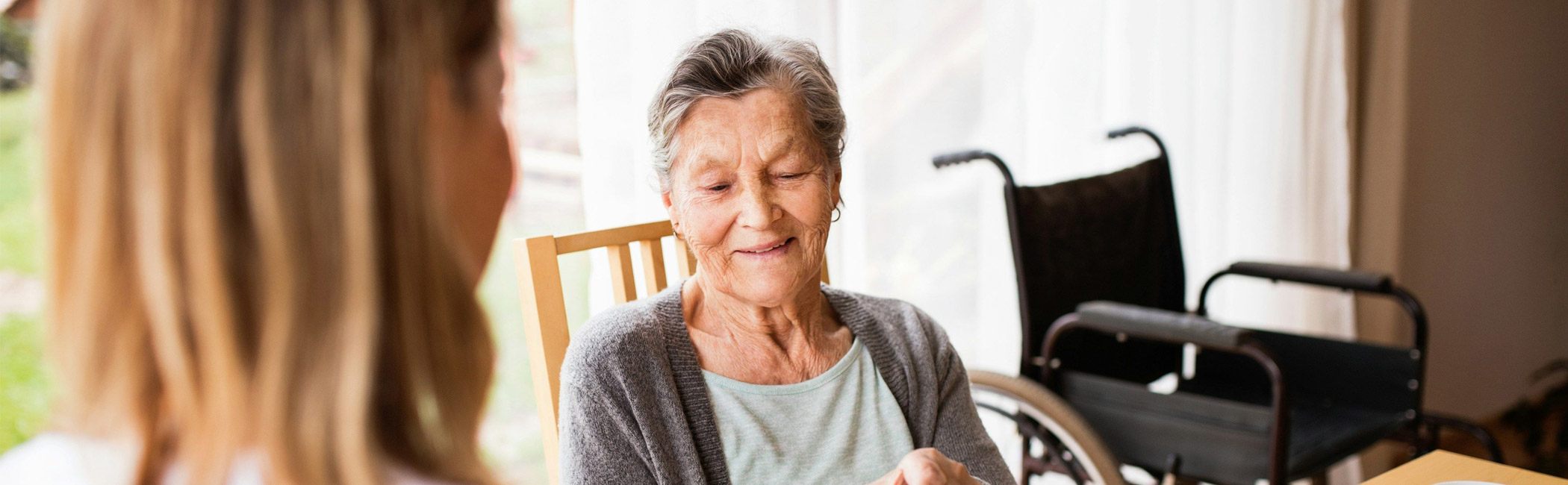 Caregiver sitting with an older woman at the table, sharing a calm and attentive conversation