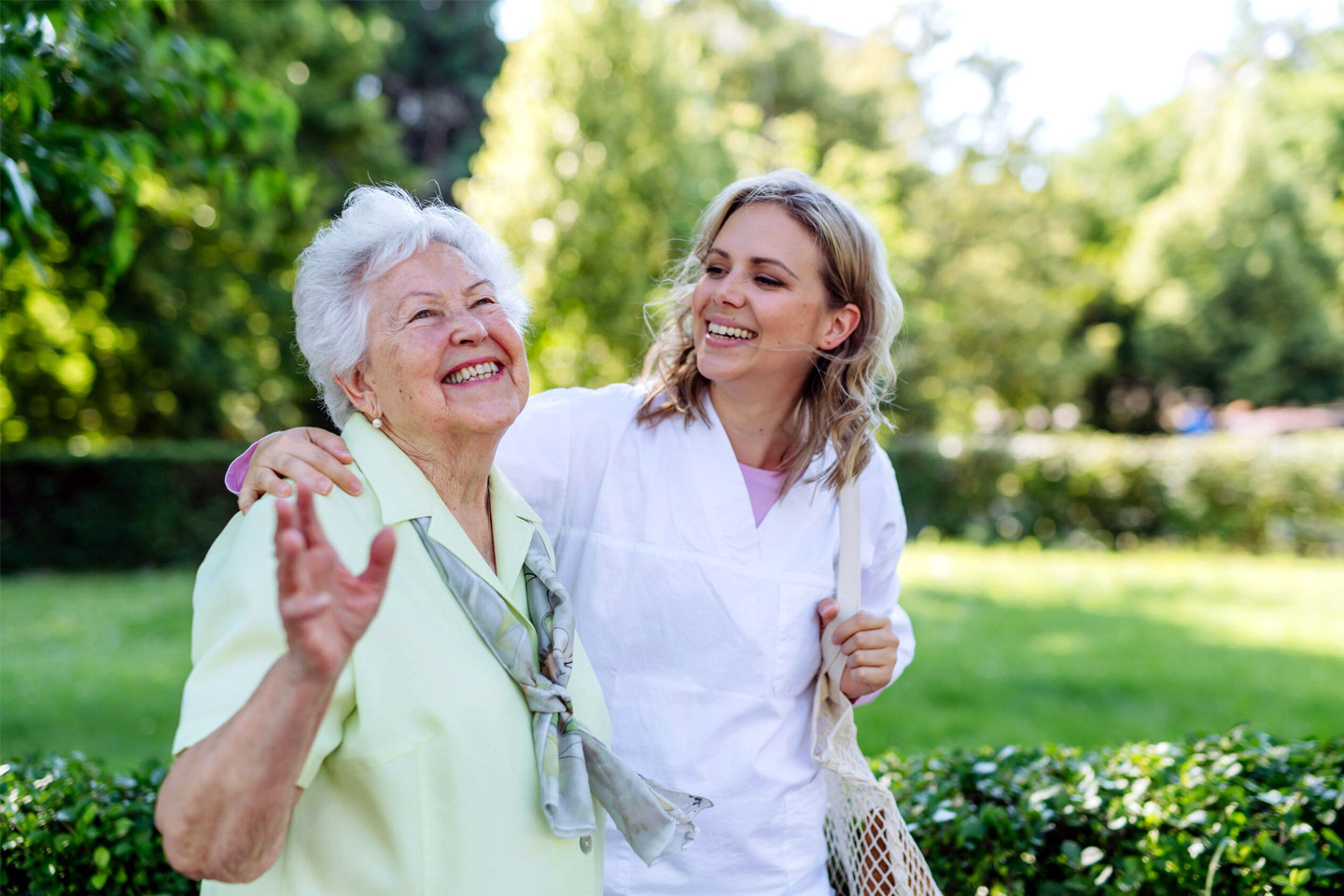 Caregiver walking beside an older woman outdoors, sharing a joyful moment and supportive companionship
